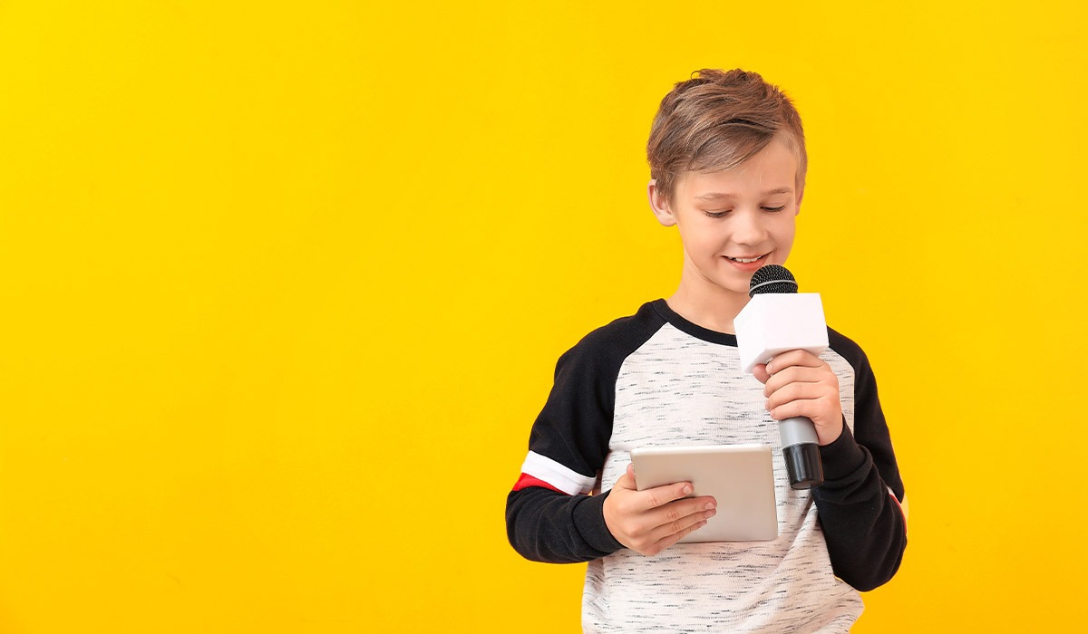 Das Foto zeigt einen Jungen. Er hält ein Mikrofon und ein Tablet in der Hand und liest auf dem Tablet.